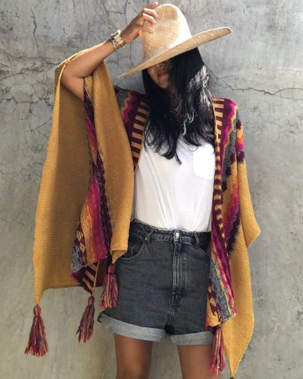 Gelber Poncho mit farbigen Mustern und Pompom Fransen an den Enden