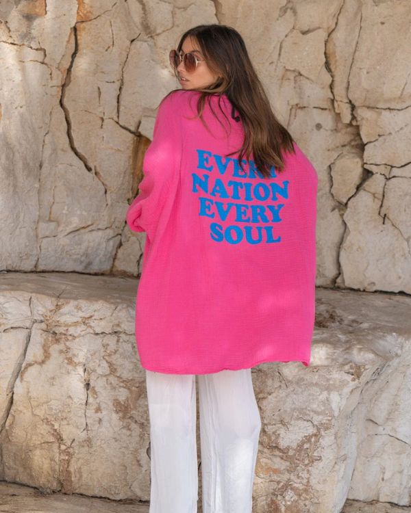 Dame trägt pinkfarbene Oversize-Bluse mit Fledermausärmeln und Aufdruck 'Every Nation, Every Soul